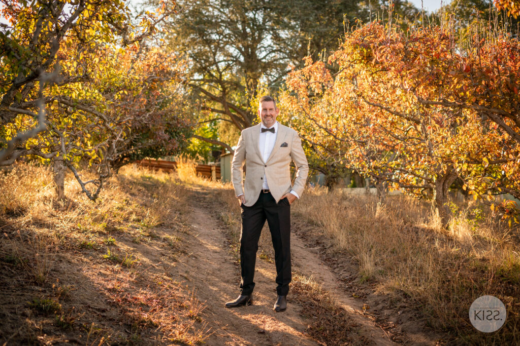 A groom standing on a path beneath autumn trees