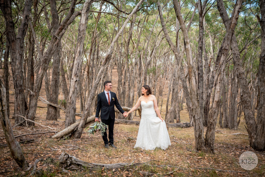 A wedding couple walking hand in hand along a forest path