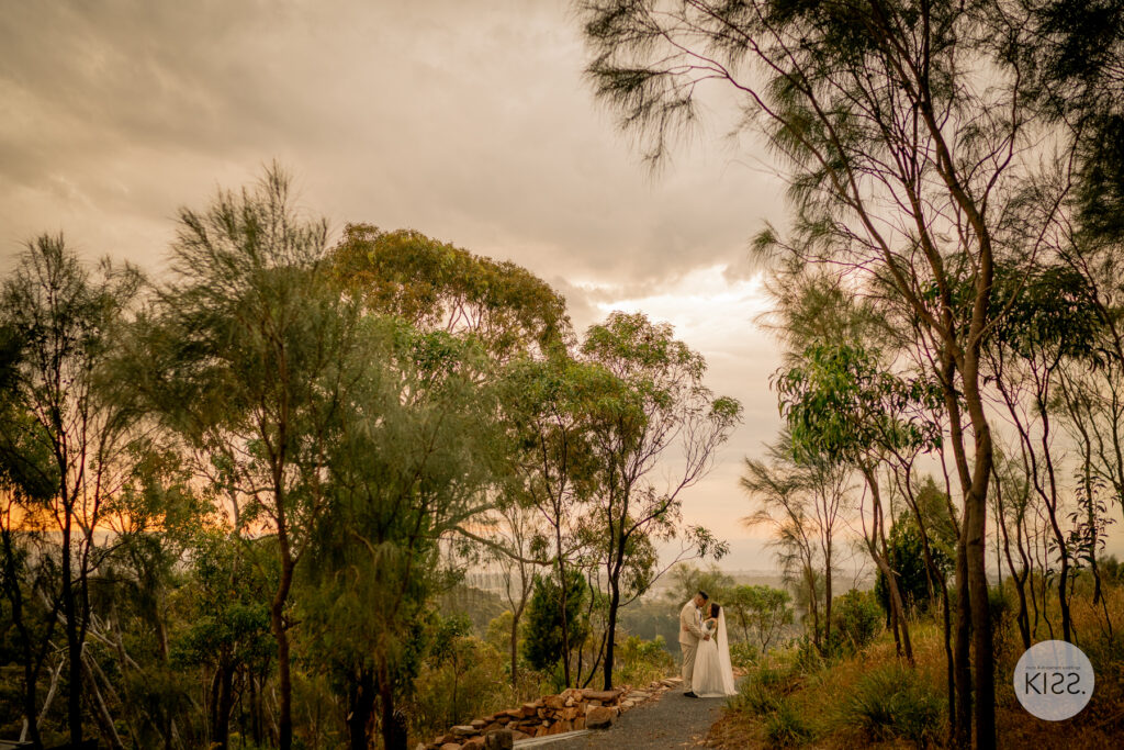 A wedding couple on a bushland path beneath a sunset sky