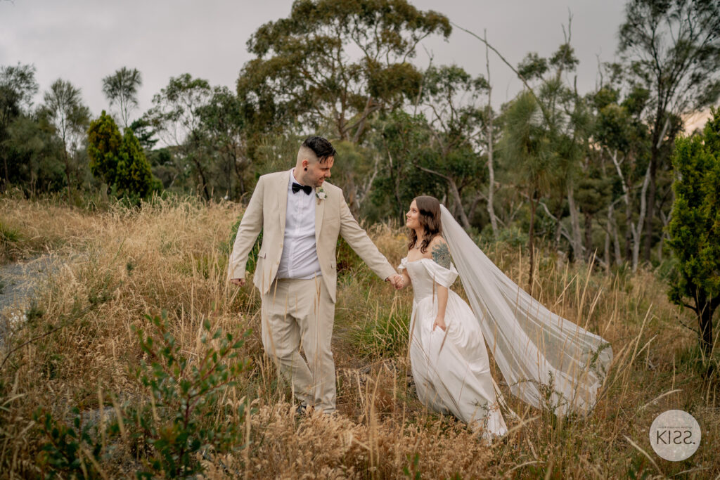 A wedding couple holding hands in tall grass