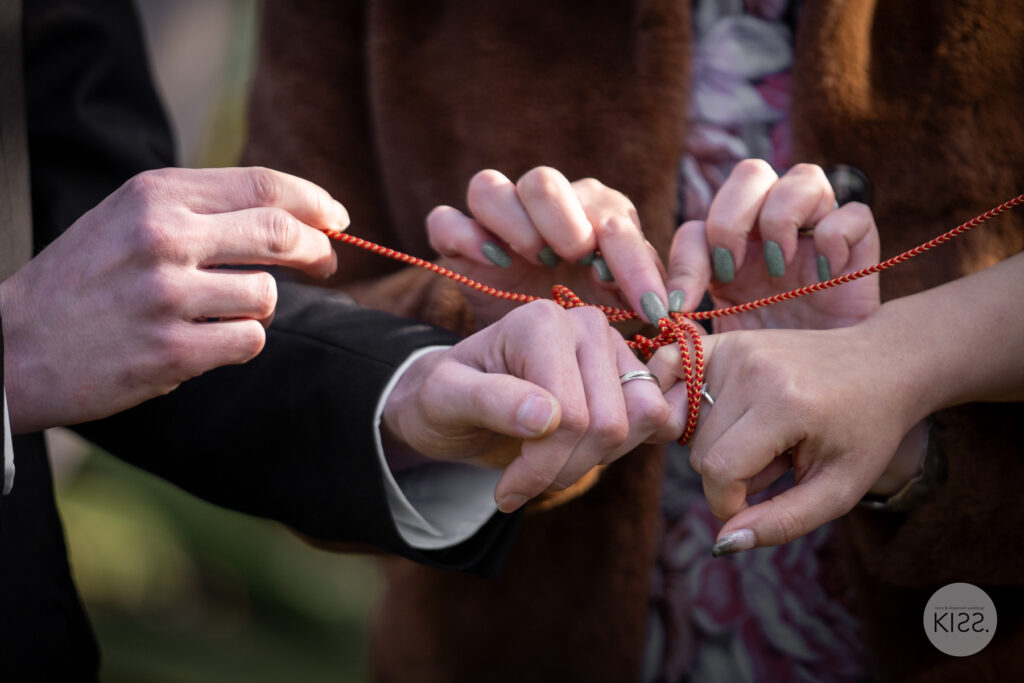 Close-up of red string being tied around a couple's hands