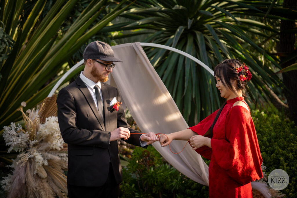 A couple holding hands during a red string wedding ceremony