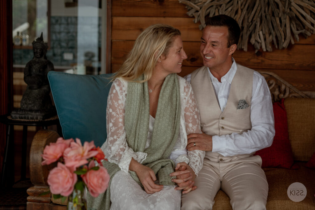 A wedding couple sitting together indoors beside their bouquet