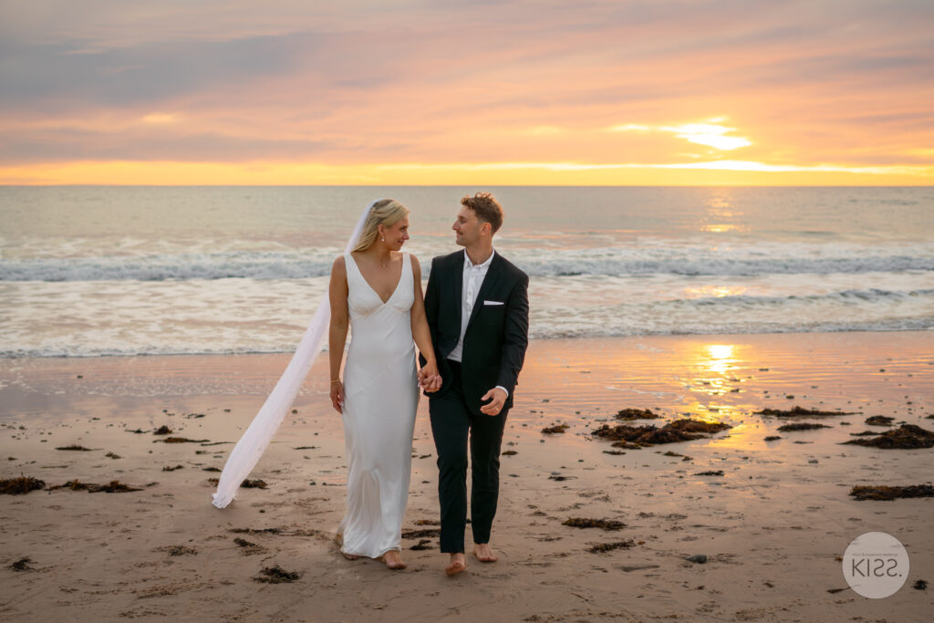A wedding couple walking along the beach at sunset