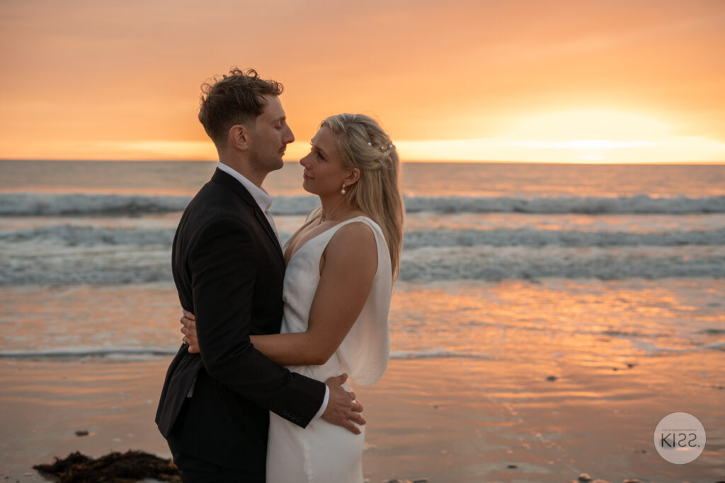 A wedding couple embracing on the beach at sunset