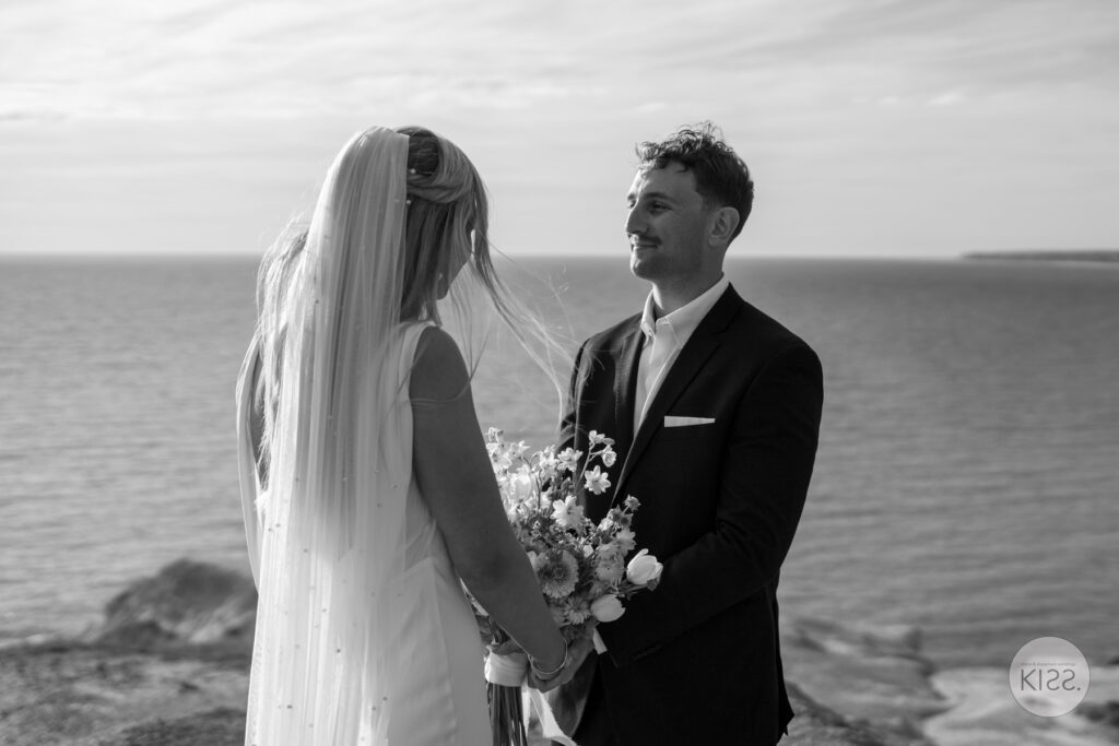 A couple holding hands during their coastal wedding ceremony in black and white