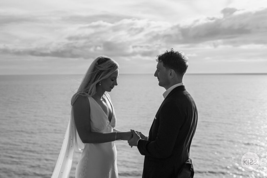 A couple exchanging rings beside the sea in black and white