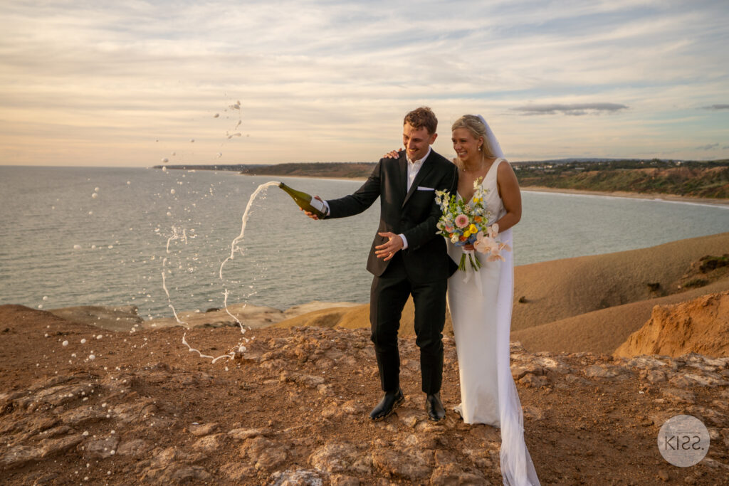 A couple celebrating with a bottle beside the coast