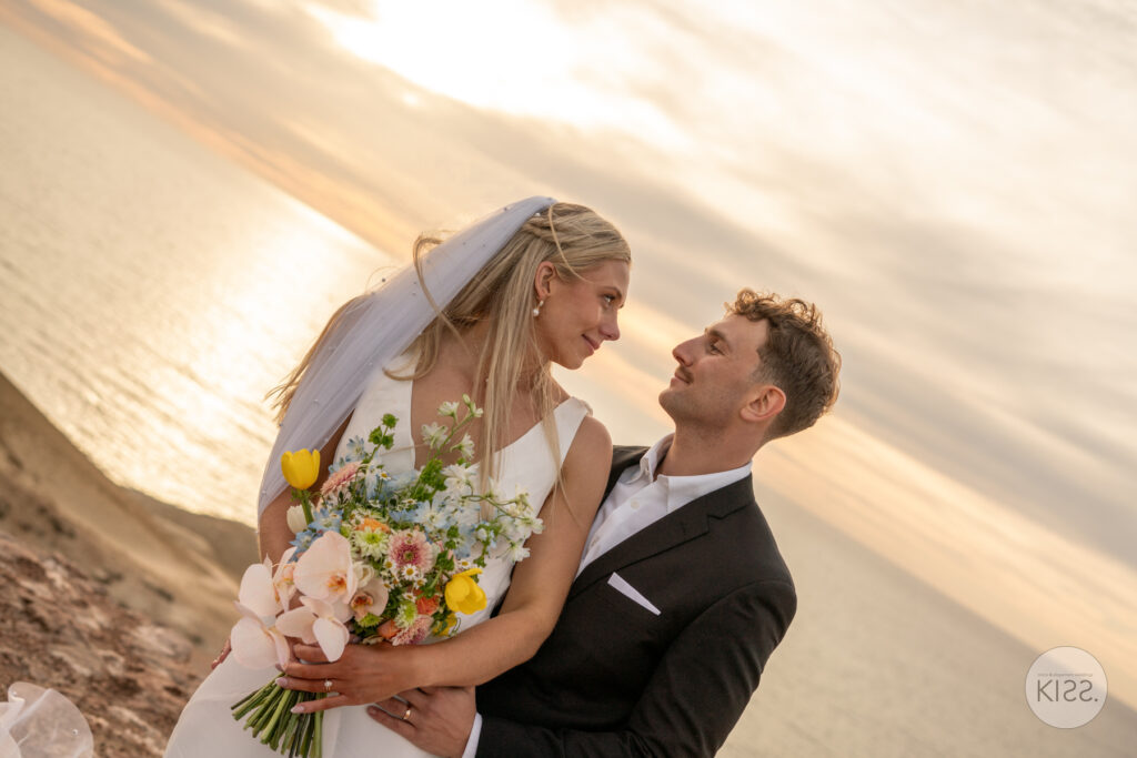 A bride and groom smiling together beside the sea
