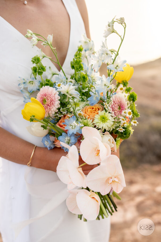 A bride holding a colourful bouquet with pink ribbon