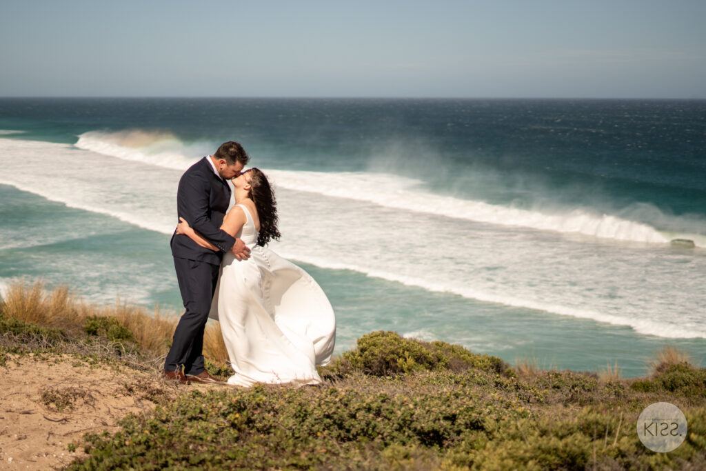 A wedding couple kissing above a turquoise coastline