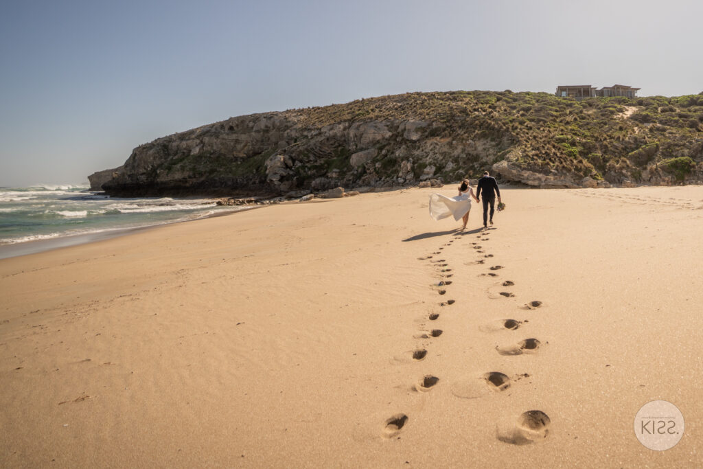 A wedding couple walking along a wide sandy beach