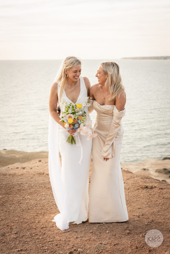 Two women in wedding dresses standing beside the coast