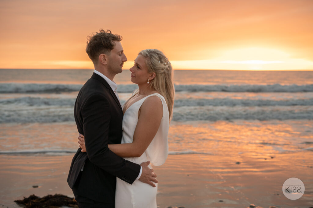 A wedding couple embracing on the beach at sunset