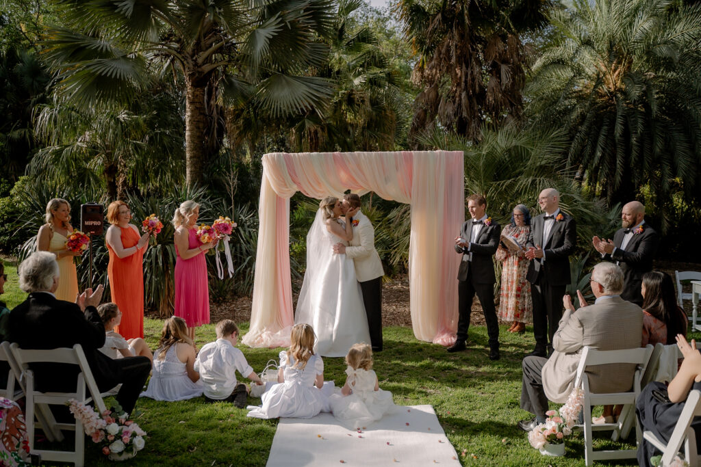 Guests watching a garden wedding beneath a draped arbour