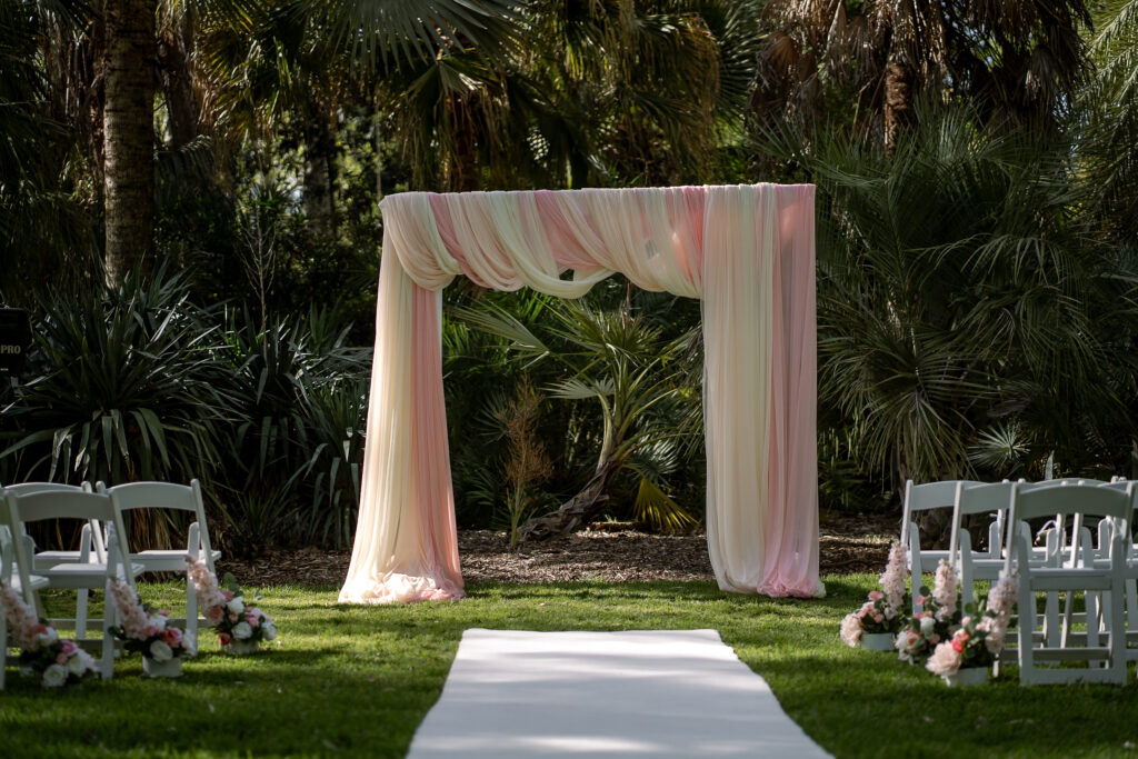 A pink and cream draped wedding arbour in a garden