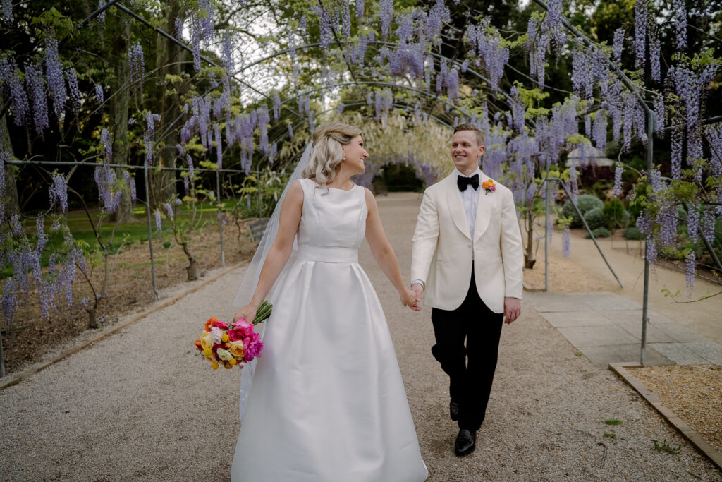 A bride and groom walking beneath flowering wisteria at Adelaide Botanic Garden