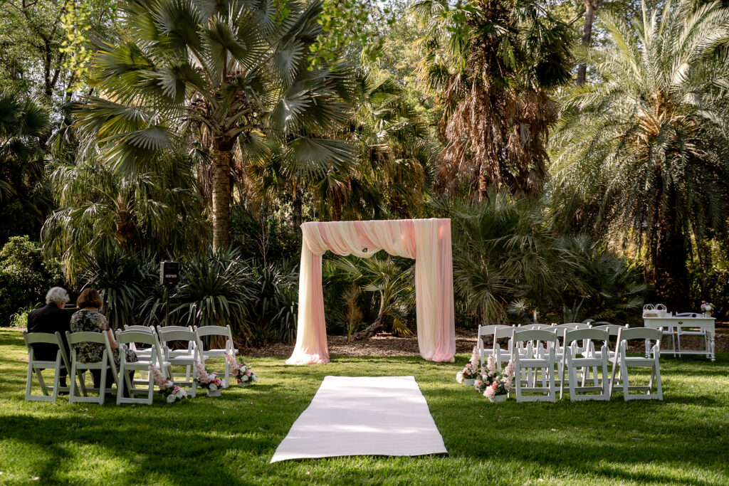 Garden wedding ceremony setup with a draped arbour and white chairs