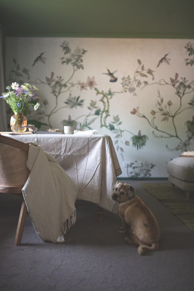 A dog beside a table and botanical wallpaper