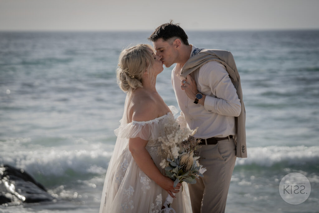 A wedding couple kissing beside the sea at Carrickalinga Beach