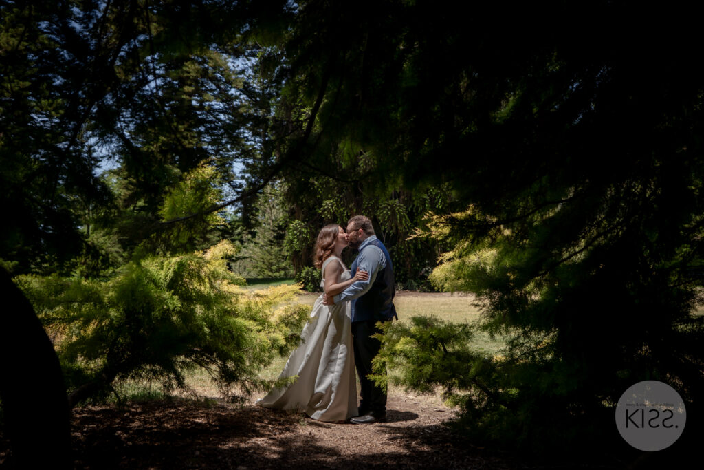 A wedding couple embracing on a shaded garden path