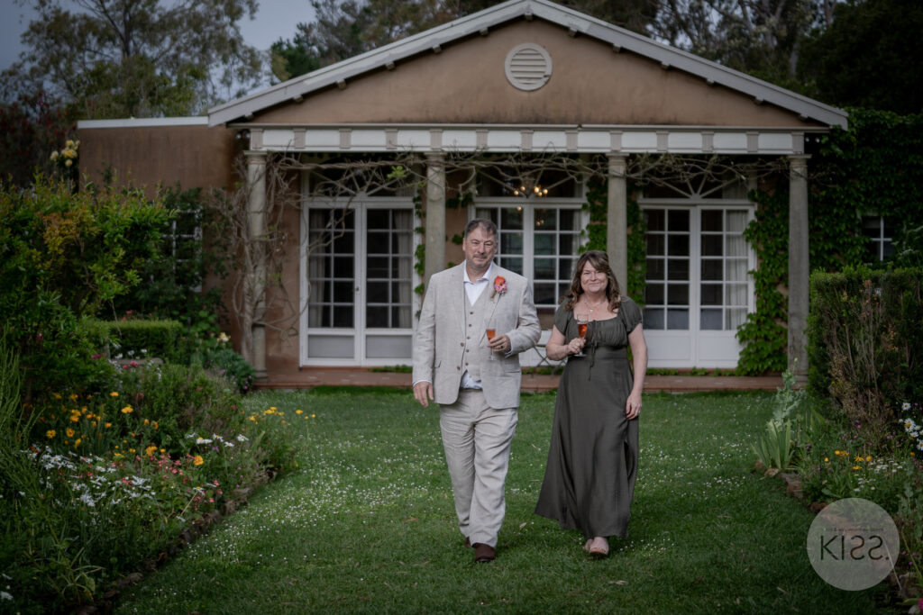 A wedding couple walking beside the glasshouse in a garden setting