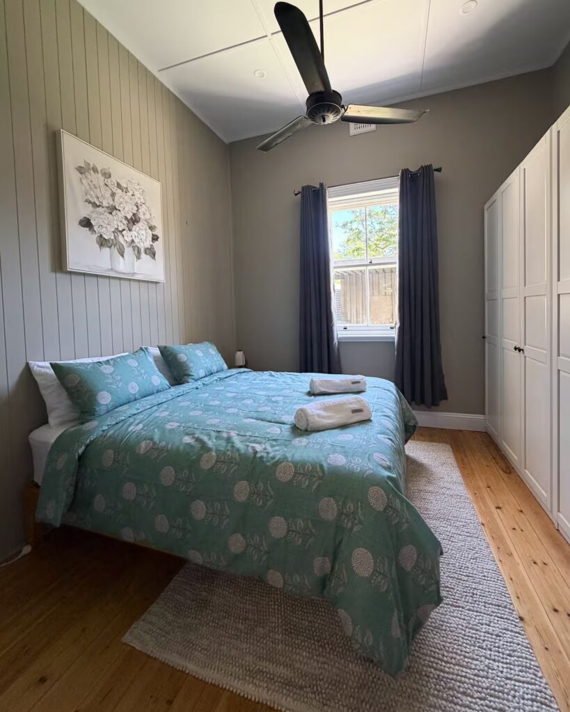 Cottage bedroom with a blue bedspread and timber floor