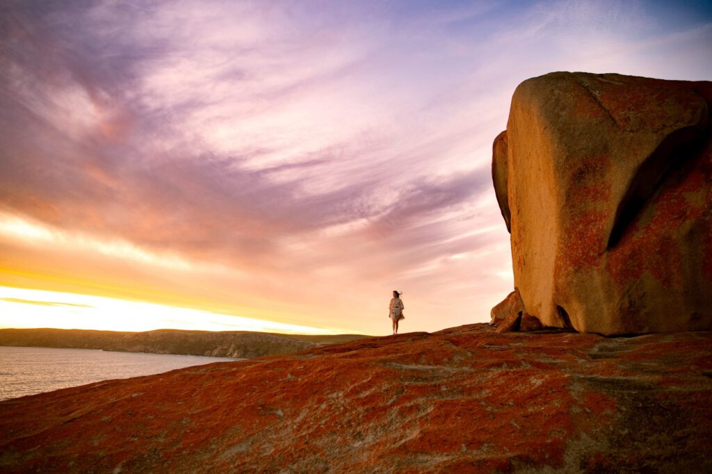 A visitor beside the granite formations at Remarkable Rocks at sunset.