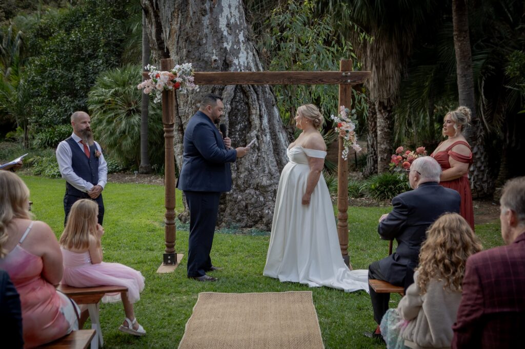 A groom reading his vows beneath a floral arch at Adelaide Botanic Garden