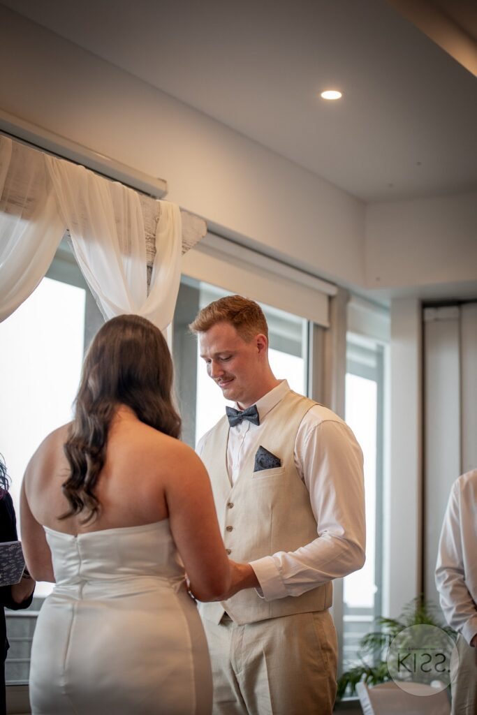 A couple exchanging vows beside a window at their indoor wedding in Glenelg