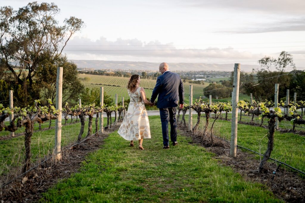 A wedding couple walking between vines with views across McLaren Vale