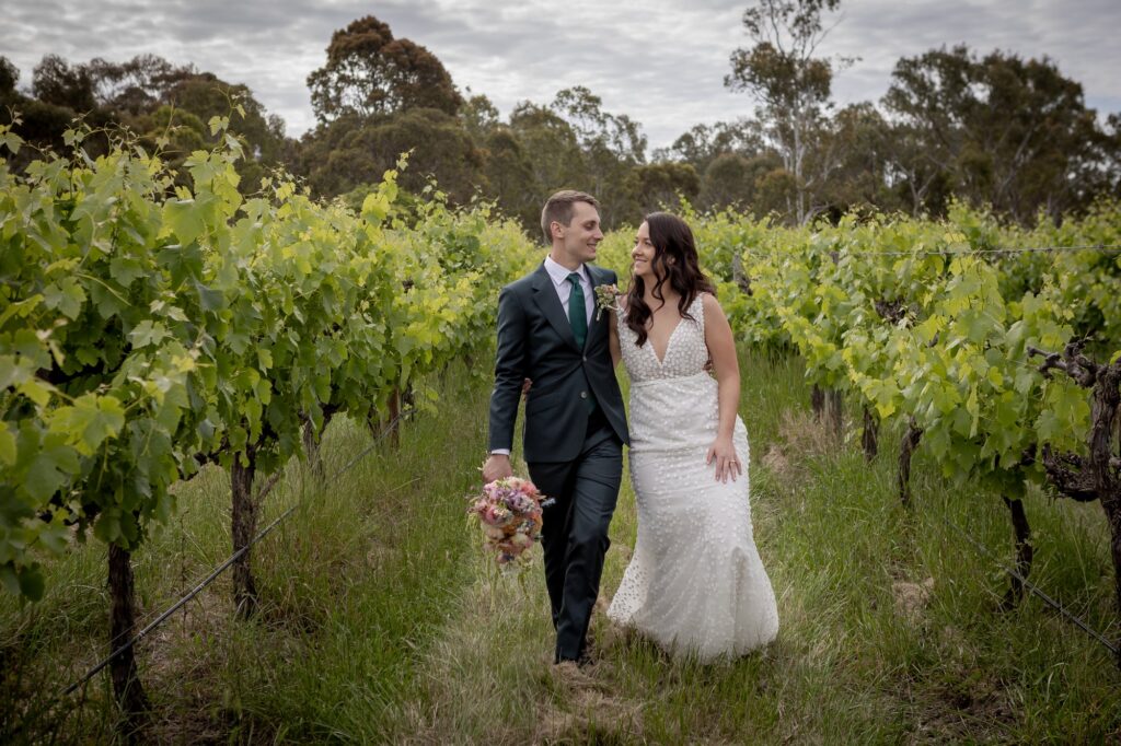 A wedding couple walking together between green vineyard rows in McLaren Vale