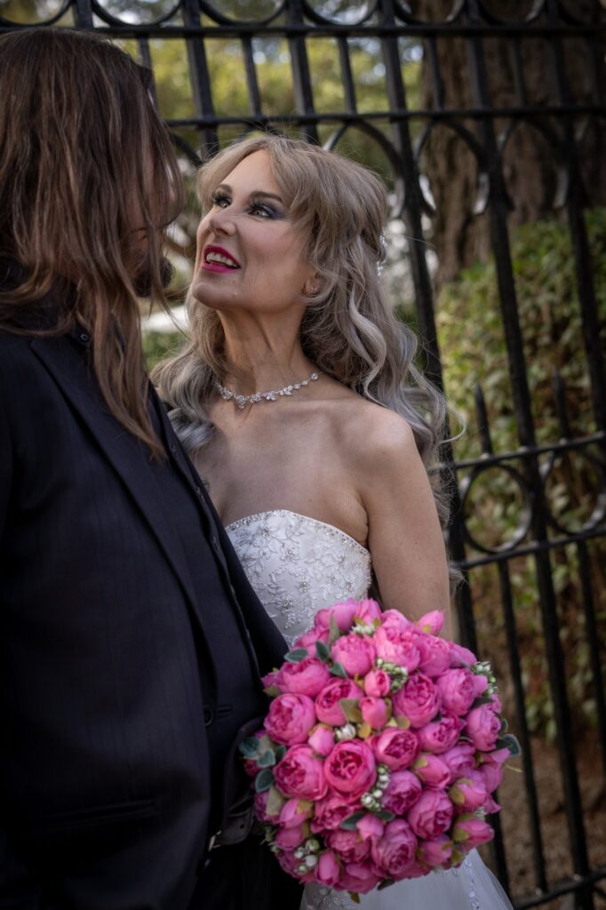 A bride smiling with a bright bouquet beside a garden gate at Thorngrove Manor