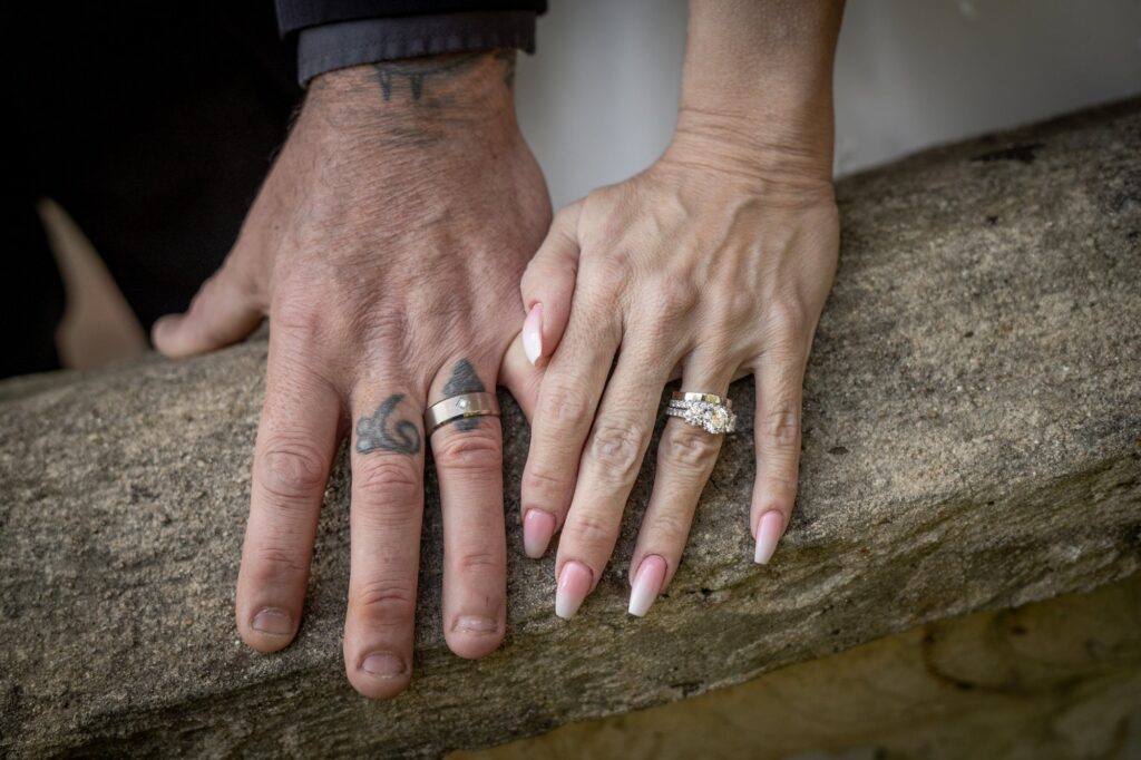 A close view of wedding rings and joined hands resting on garden stonework